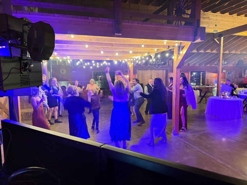 Guests dancing in a rustic event room with warm string lights and DJ lighting